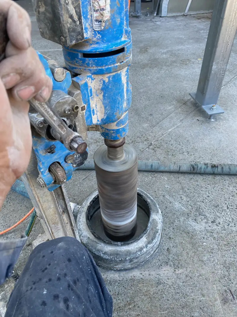 Core drill barrel cutting into a concrete slab, water fed to keep the dust down
